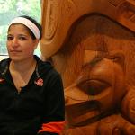 Female student sitting next to Native American carvings